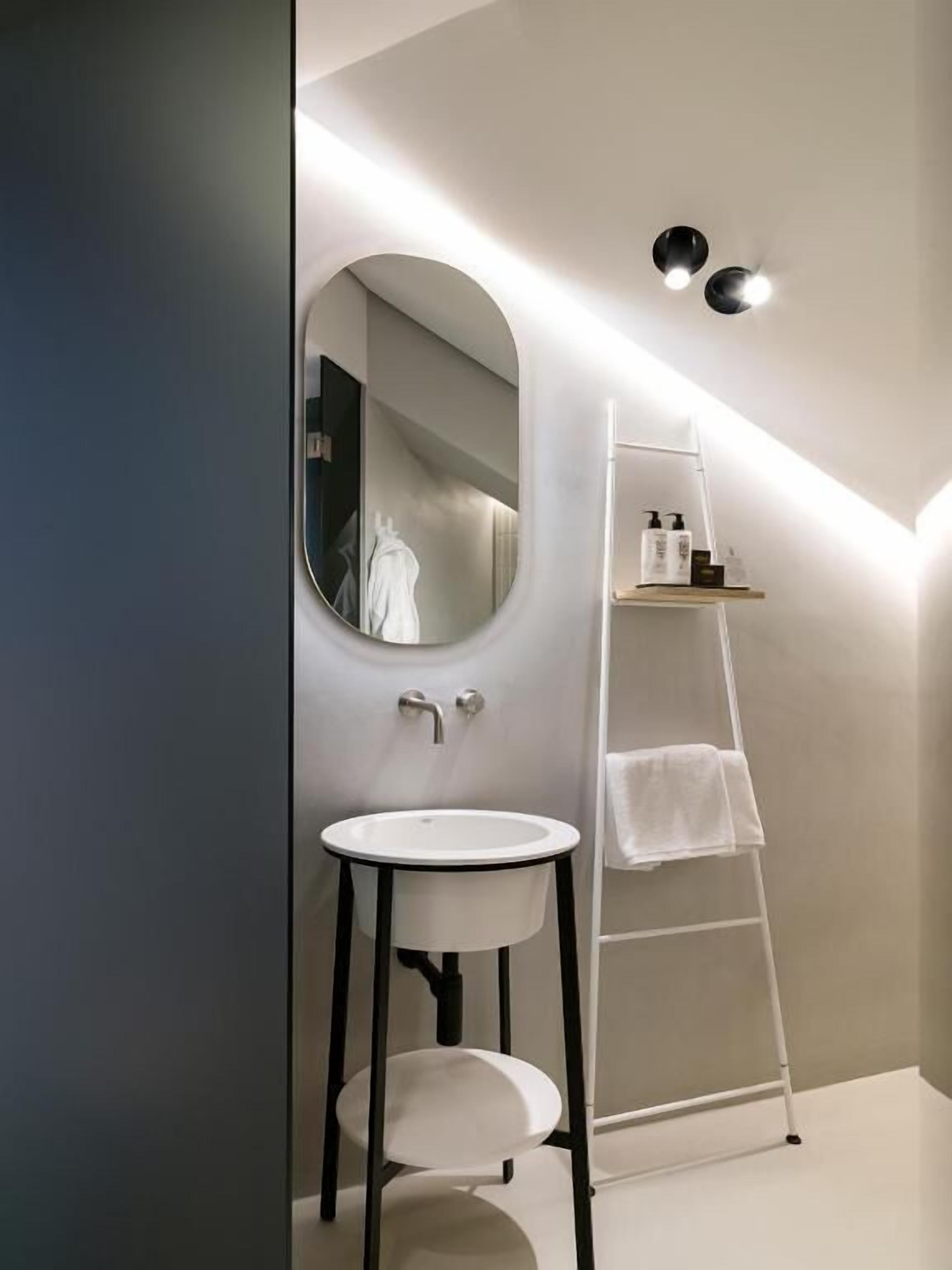 Une salle de bain moderne avec un miroir rond, un lavabo blanc et un porte-serviettes blanc.