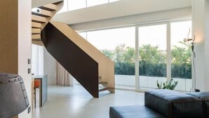 Ein modernes Interieur mit einer einzigartigen Wendeltreppe, einem Ecksofa und großen Fenstern mit Blick auf Grünflächen.
