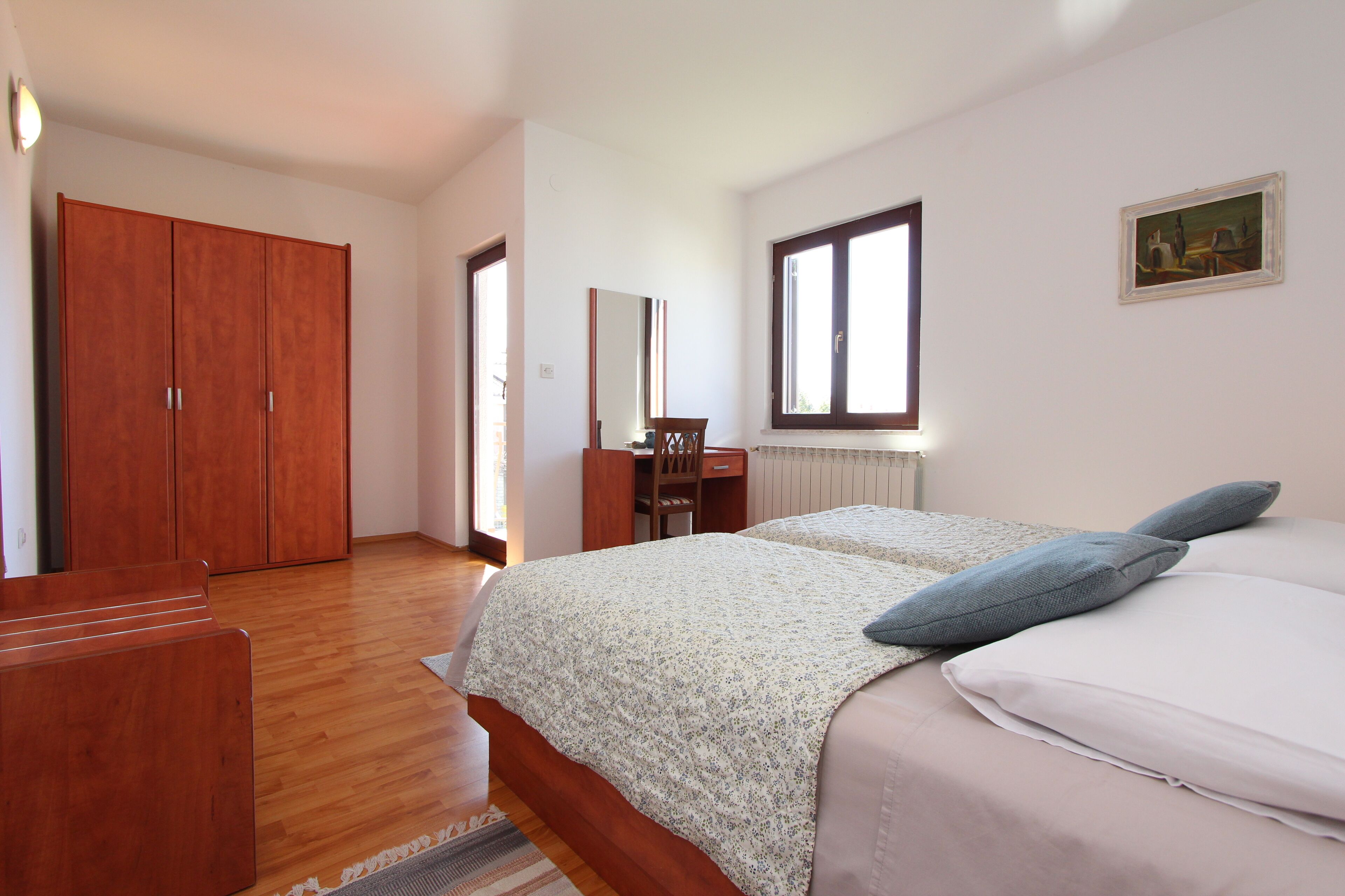 Un dormitorio con un armario de madera, un escritorio, una cama con colcha estampada y un ventanal.