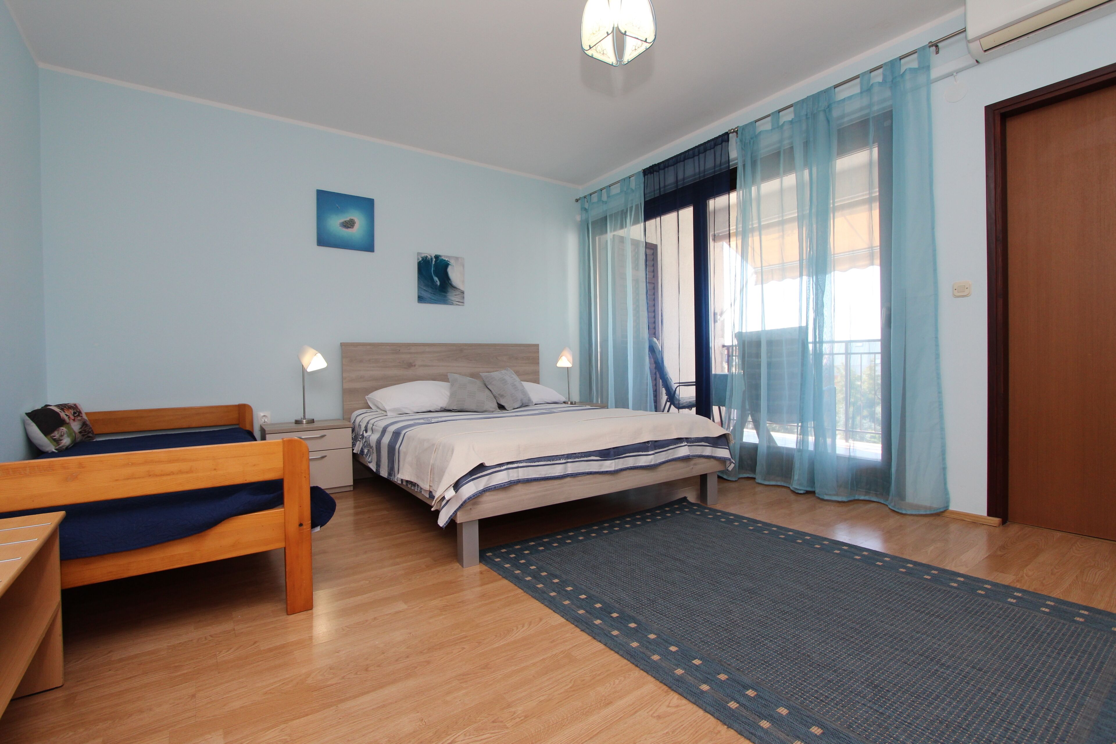 Een slaapkamer met een bed, een bureau, een stoel, een nachtkastje en een raam met gordijnen.