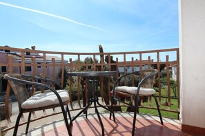 Een balkon met twee rieten stoelen en een klein tafeltje, met uitzicht op een tuin en gebouwen.
