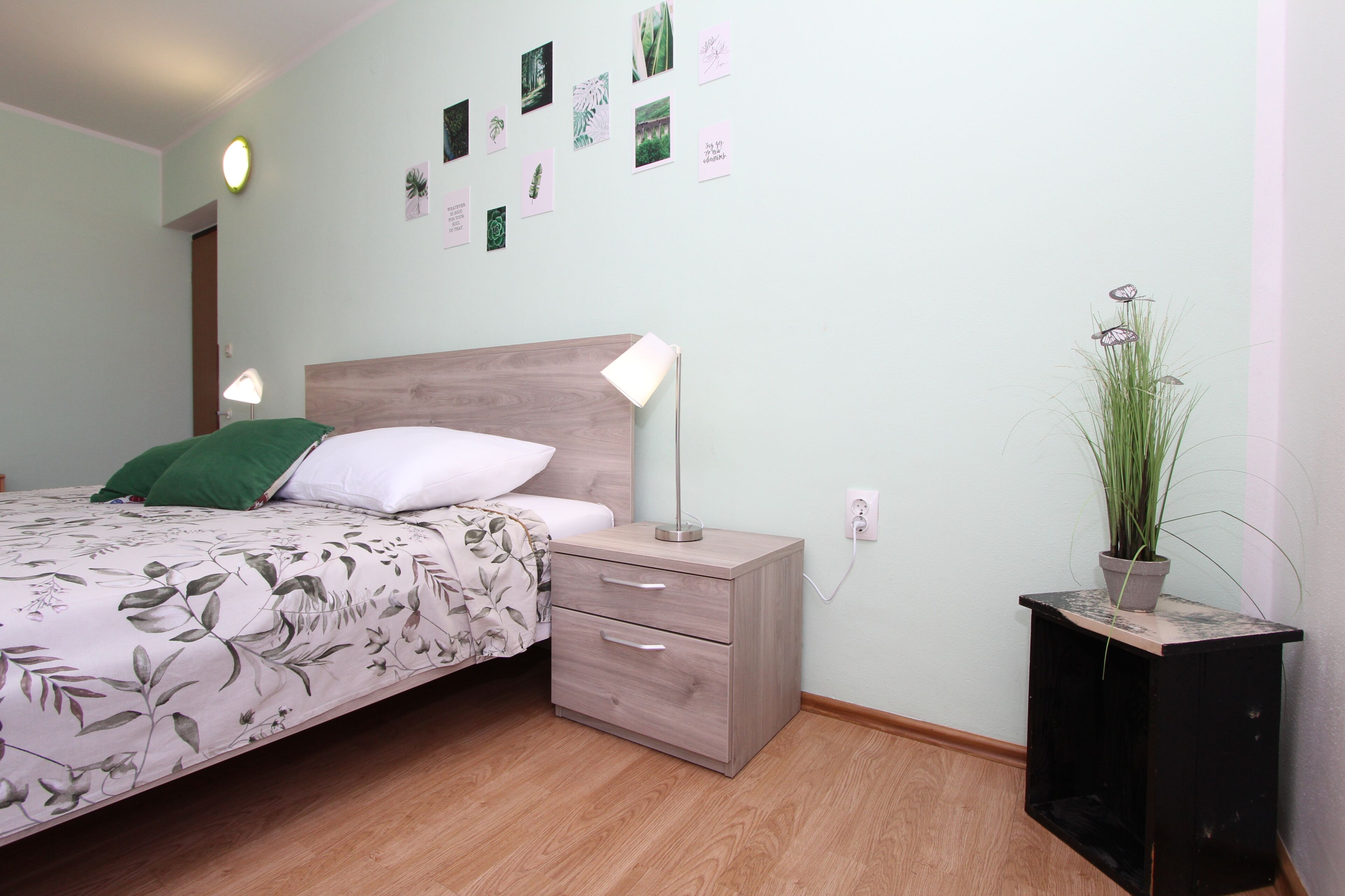 A bedroom with a bed, bedside table, lamp, wall art, and a potted plant.
