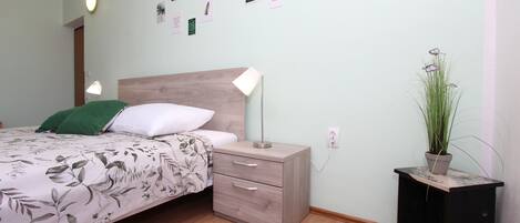 A bedroom with a bed, bedside table, lamp, wall art, and a potted plant.