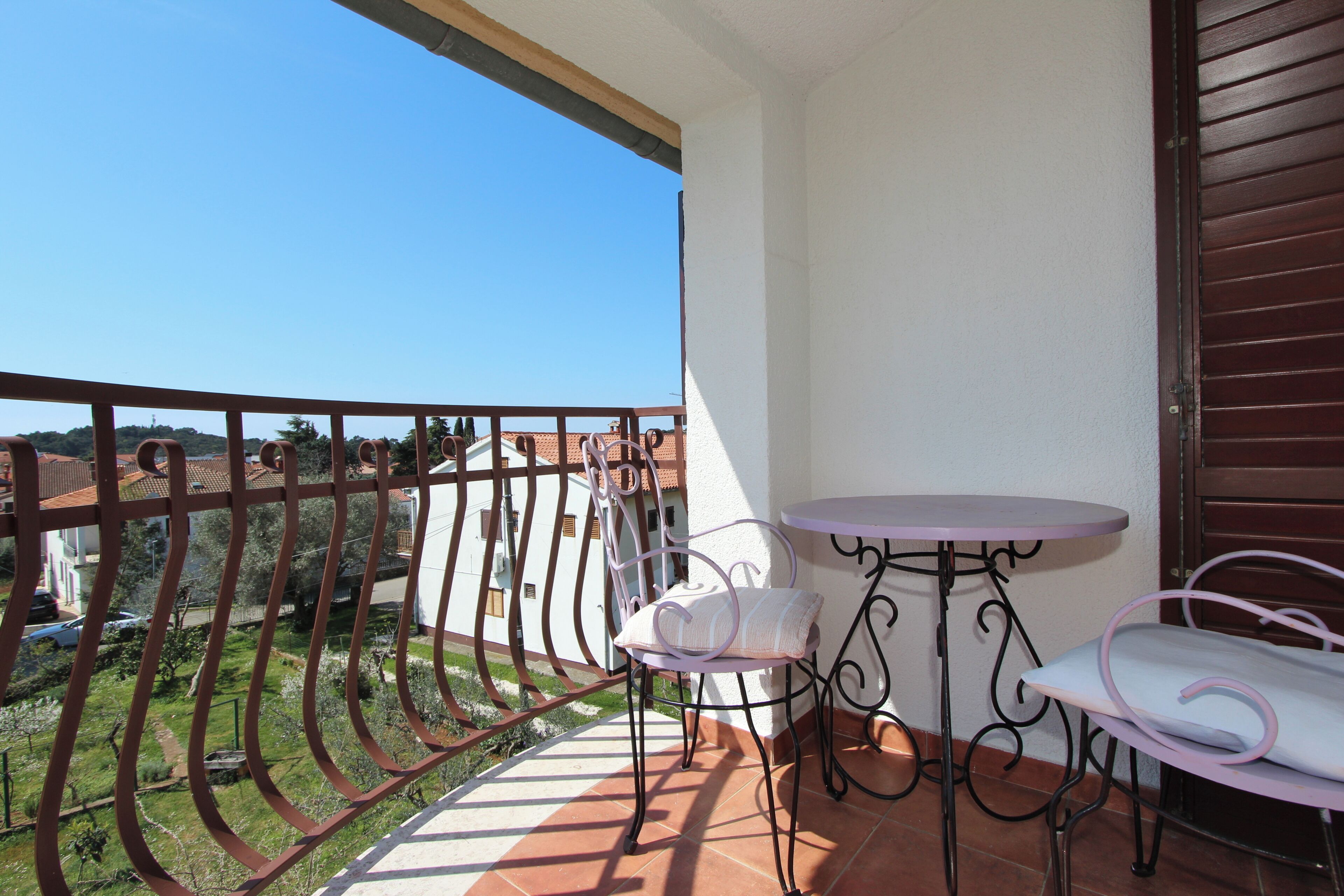 Un balcón con vistas a casas, una mesita y dos sillas.