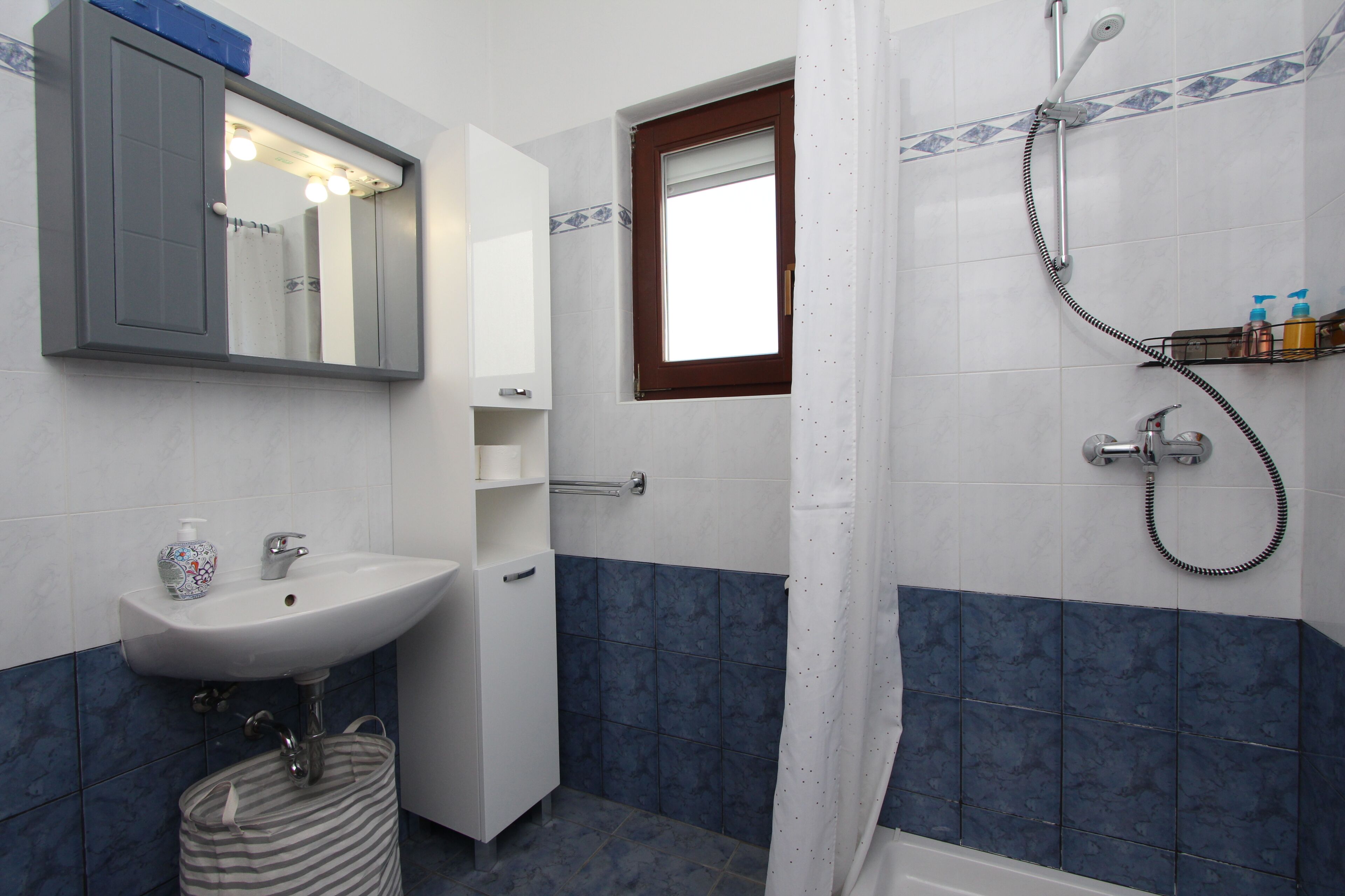 A bathroom with a sink, mirror, shower, and a window.