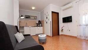 A modern living room with a sofa, a small round table, a kitchen area with cabinets and a microwave, and a TV mounted on the wall.