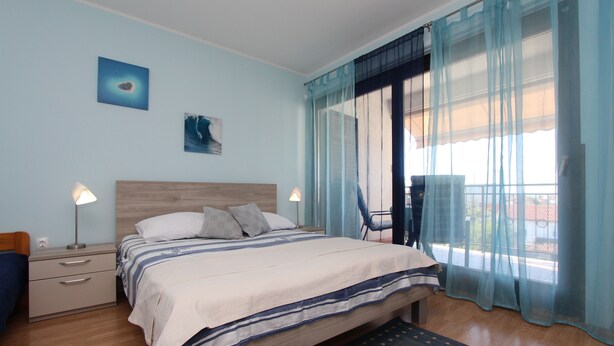 A bedroom with a bed, nightstands, a chair, and a view of the outdoors.