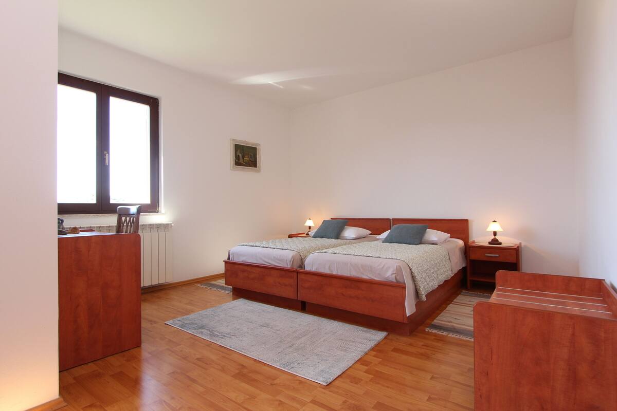 A bedroom with a double bed, bedside tables, a desk, and a window.
