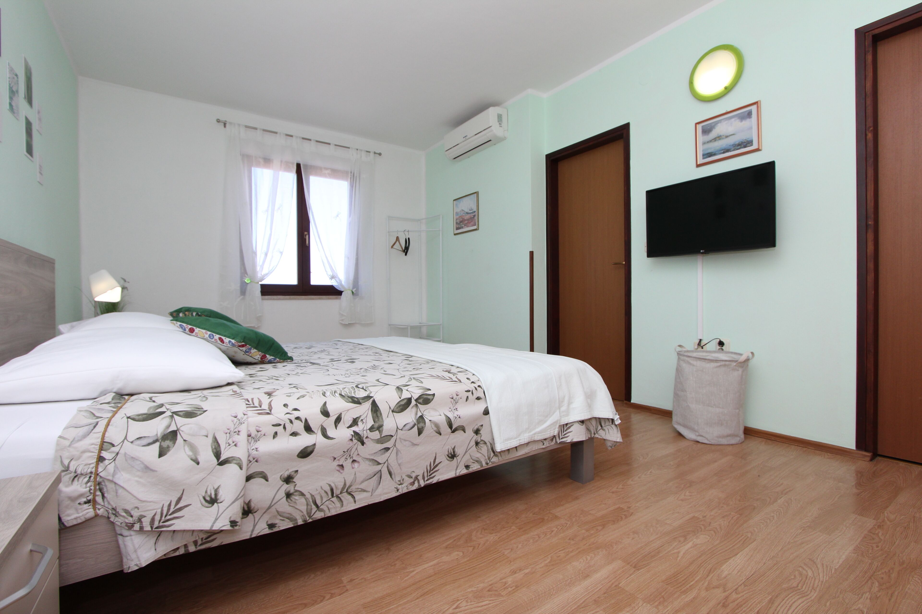 A bedroom with a bed, a television mounted on the wall, a window with curtains, and a door.
