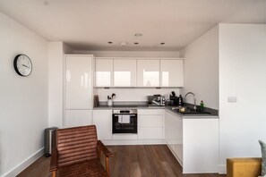 Una cocina compacta con armarios blancos, horno integrado y un lavamanos.