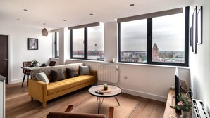 Ein modernes Wohnzimmer mit einem gelben Sofa, einem runden Couchtisch und großen Fenstern mit Blick auf die Stadt.