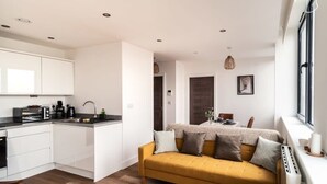 Eine moderne Küche mit weißen Schränken, einem gelben Sofa und einem Essbereich mit Tisch und Stühlen.