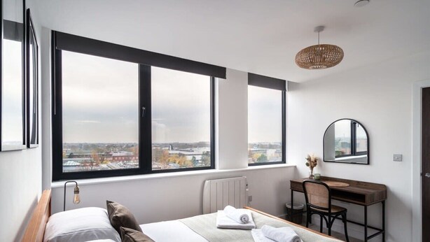 Ein modernes Schlafzimmer mit großem Fenster, einem Bett, einem Schreibtisch und einem Spiegel.