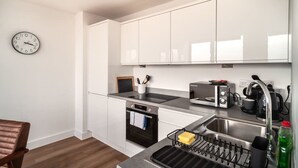 Eine moderne Küche mit weißen Schränken, einer Edelstahlspüle, einem eingebauten Backofen und einer Wanduhr.