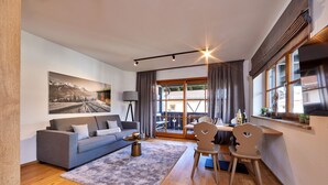 A modern living room with a sofa, coffee table, and a painting of a mountain landscape. - Stylish Alpine Retreat for 4 – Walk to Slopes with Alpspitze Views & Balcony (Garmisch-Partenkirchen)