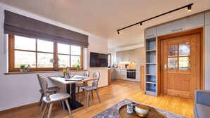 A modern kitchen with a dining area, wooden flooring, and a large window. - Stylish Alpine Retreat for 4 – Walk to Slopes with Alpspitze Views & Balcony (Garmisch-Partenkirchen)