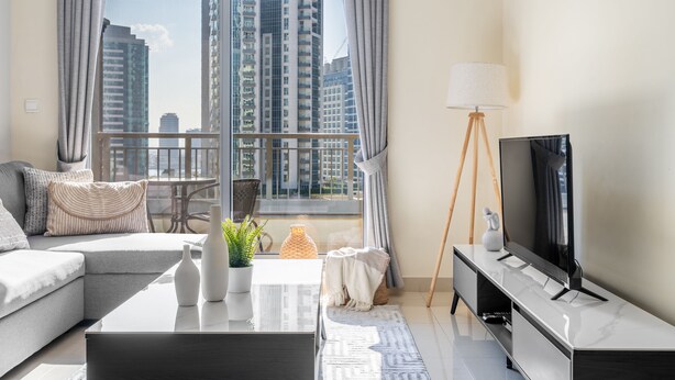 A modern living room with a sofa, coffee table, TV, and a view of tall buildings through a large window. - The Burj Khalifa Collection (Dubai)