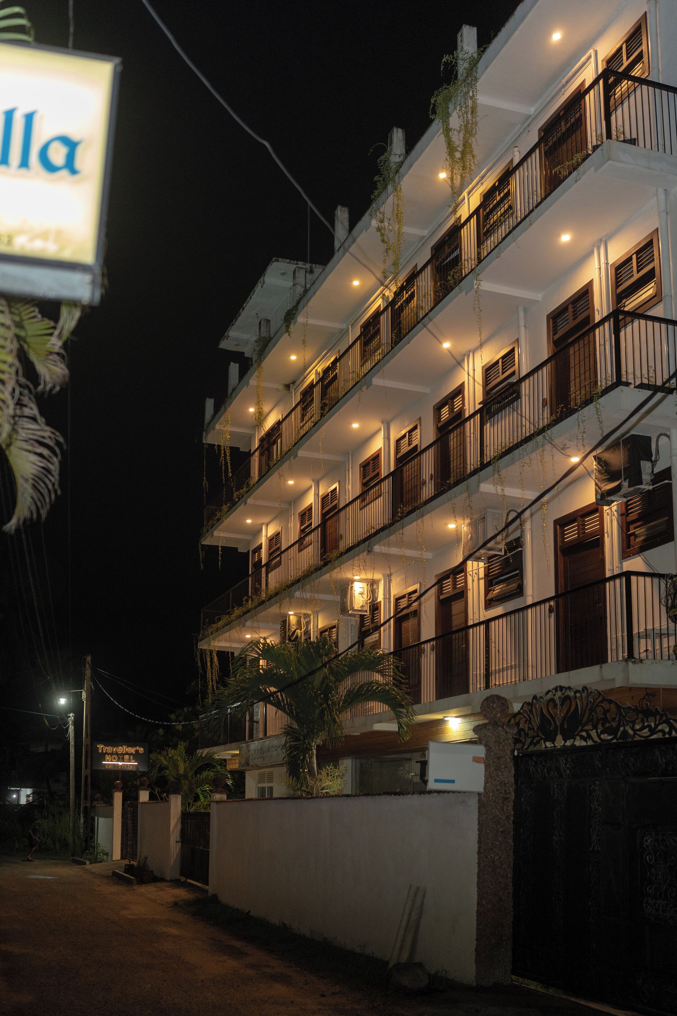 A multi-story hotel with balconies, a well-lit entrance, and a signboard.