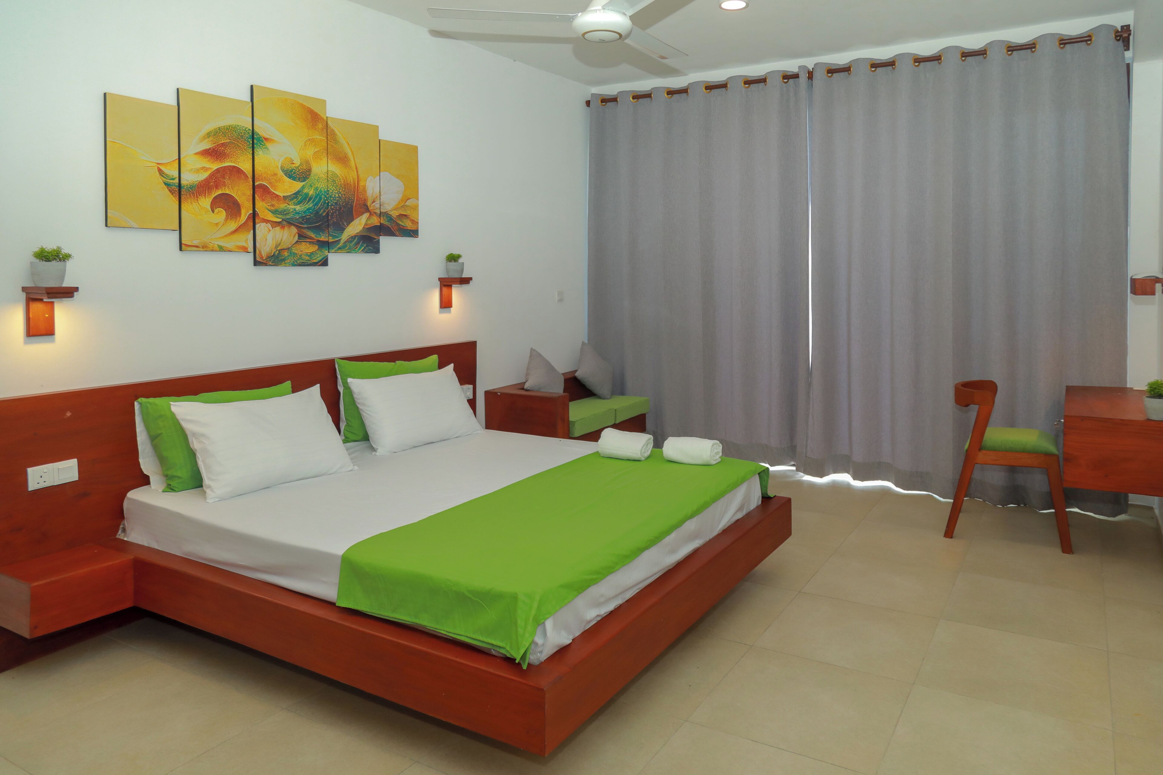 A hotel room with a large bed, a desk, a chair, and a ceiling fan.