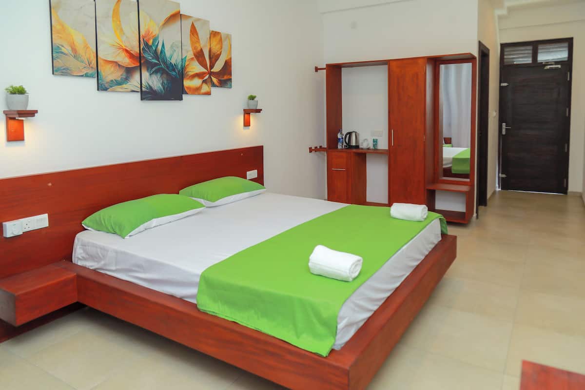 Une chambre d’hôtel avec un lit en bois, une couvre-lit verte, du linge de lit blanc, une armoire en bois et un miroir.