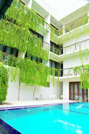 Une piscine à l’eau d’un bleu cristallin, entourée de murs blancs et de balcons ornés de plantes retombantes.