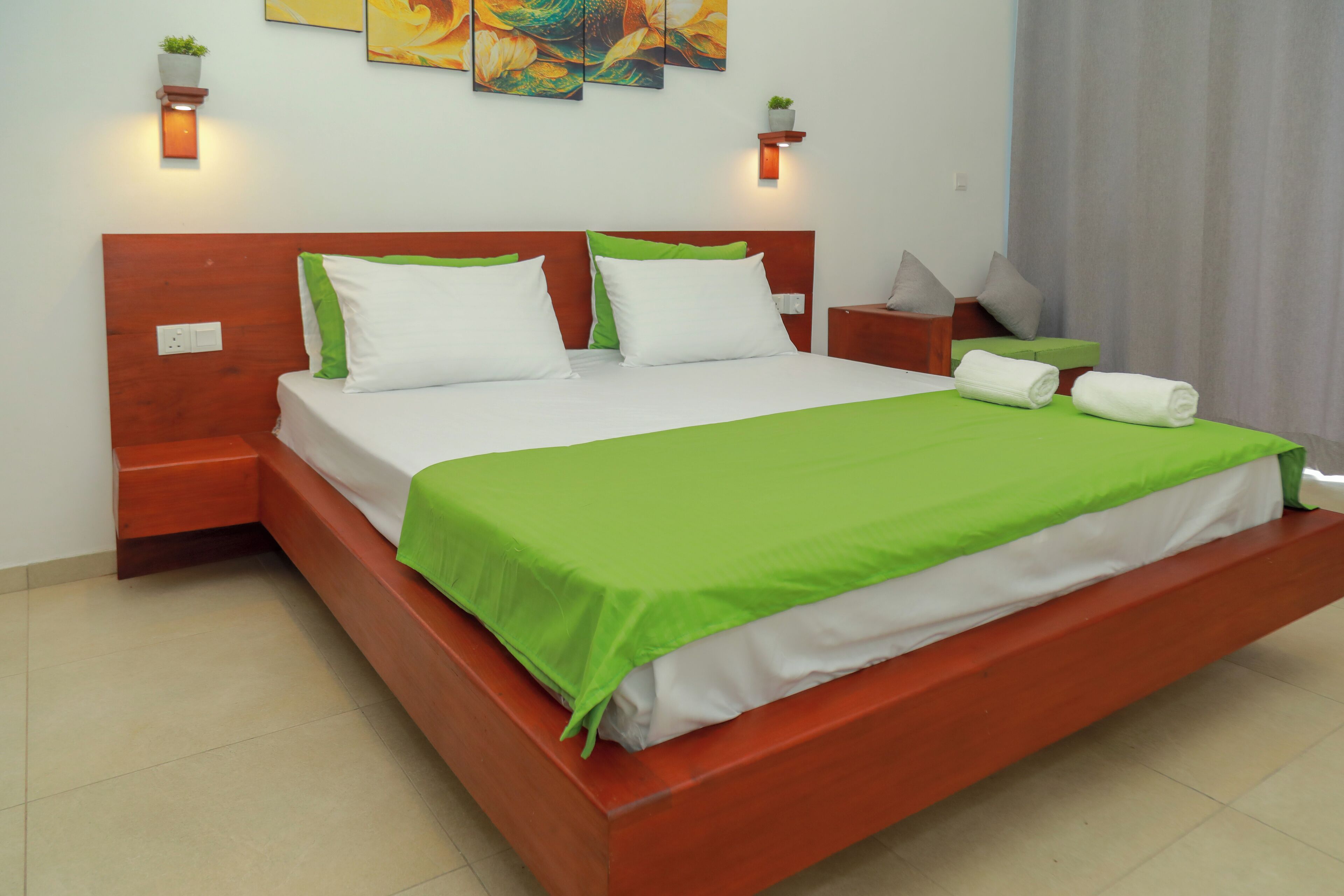 A neatly made bed with green bedding, a wooden headboard, and two bedside tables with lamps.