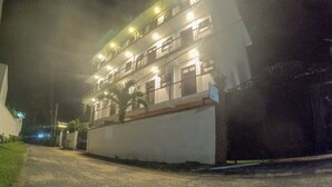 Un immeuble à plusieurs étages doté de balcons, d’une allée gravillonnée et d’une entrée fermée par un portail.