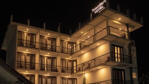 Un hôtel à plusieurs étages, doté de balcons, d’une enseigne indiquant « Hôtel des Voyageurs » et d’une façade bien éclairée.