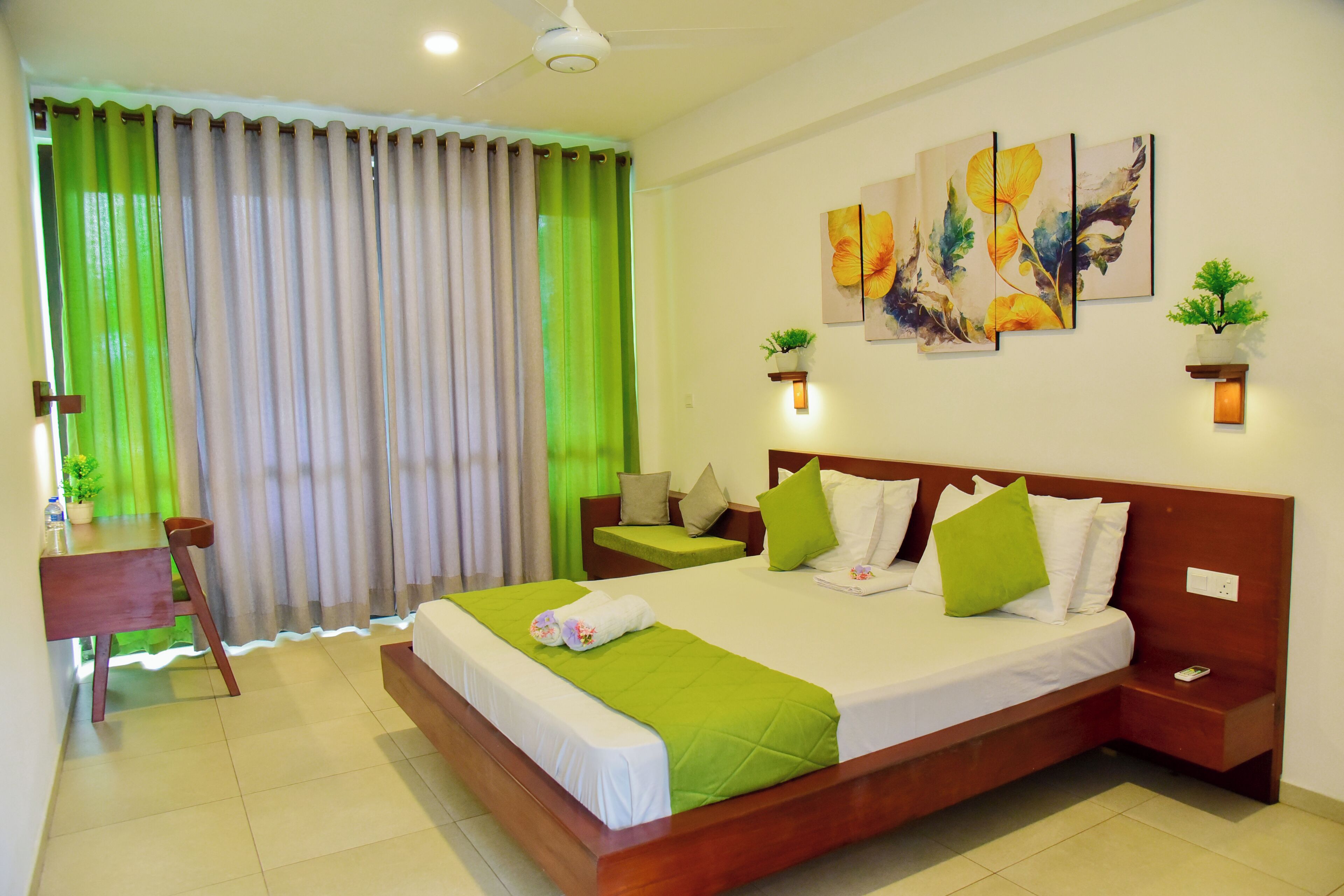 A hotel room with a large bed, a desk, a chair, a nightstand, a wall-mounted plant, and artwork on the wall.