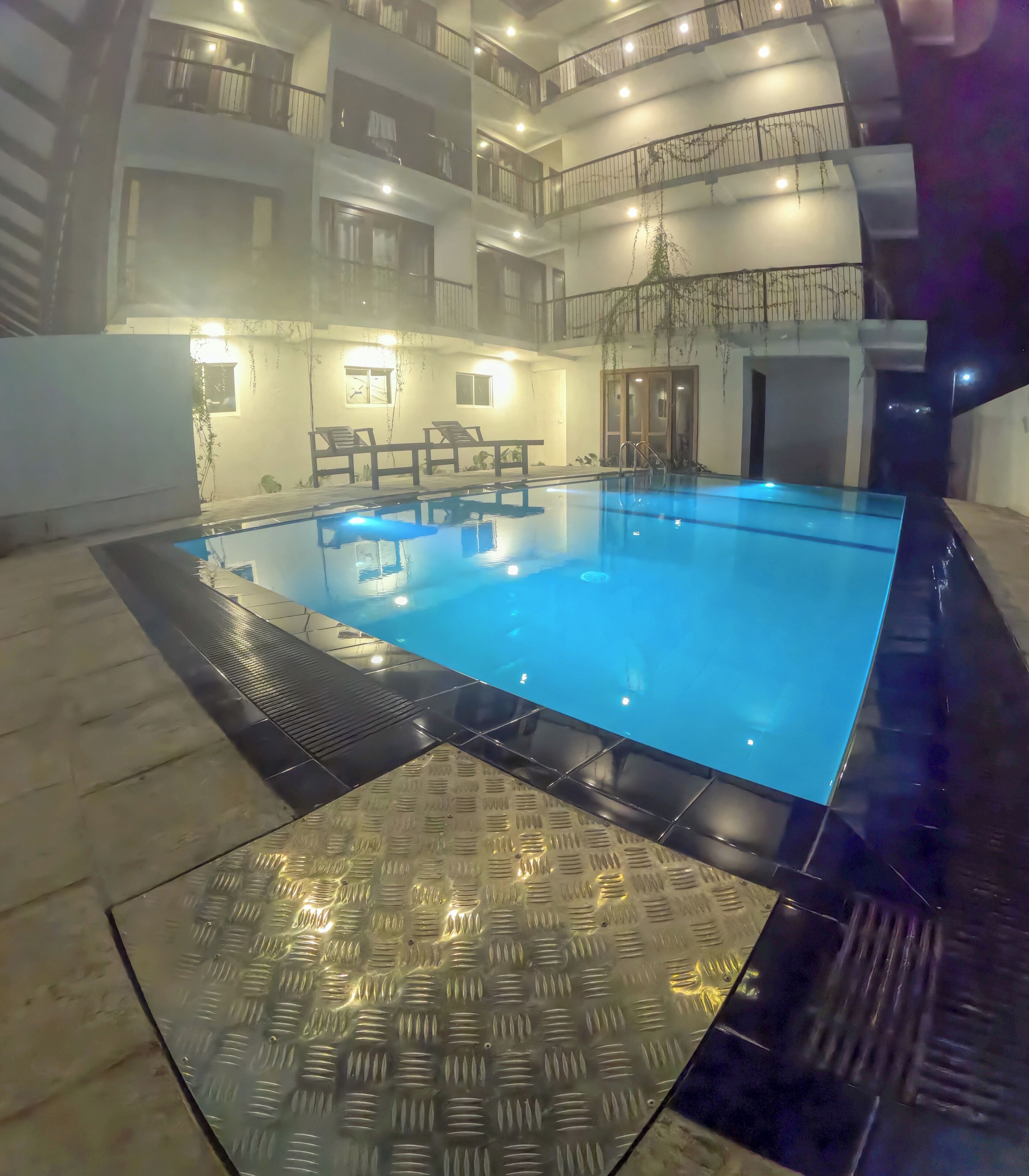 Ein Schwimmbecken mit Fliesen umgeben, umgeben von einem mehrstöckigen Gebäude mit Balkonen und Geländern.