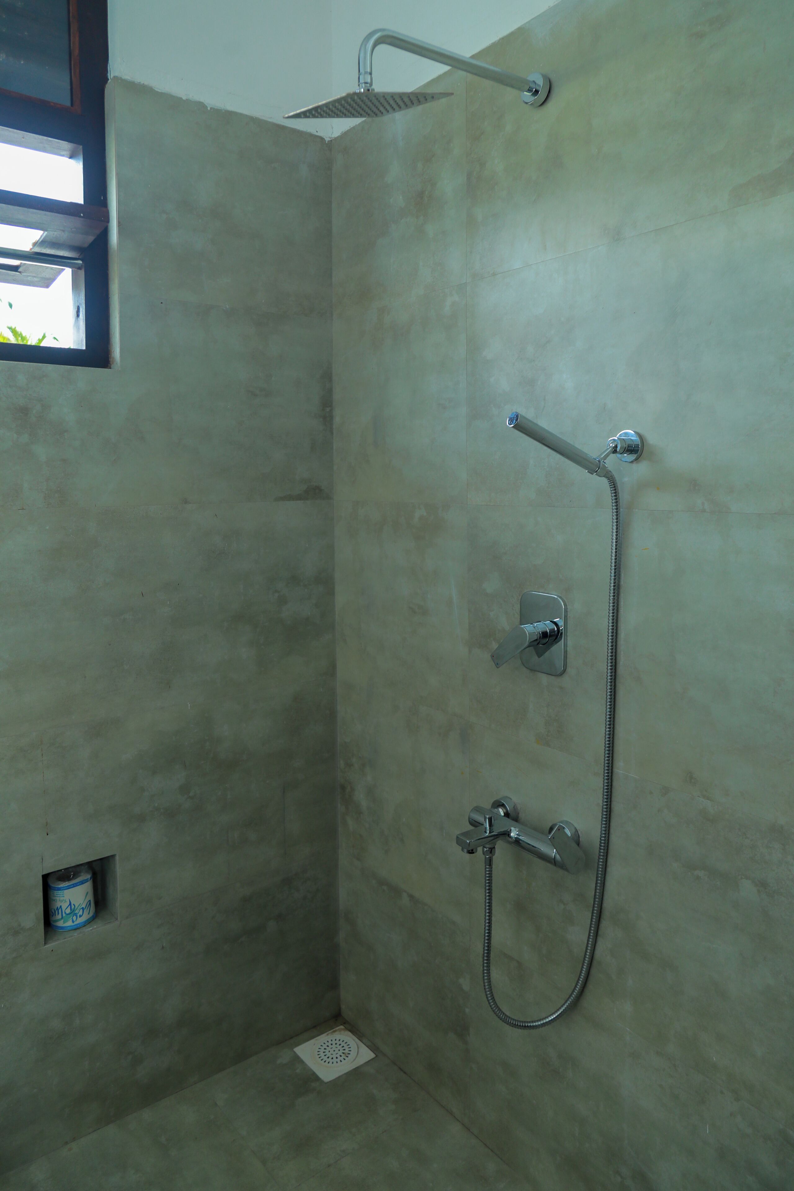 Ducha con cabezal de ducha de mano, grifo empotrado en la pared y desagüe en el suelo.