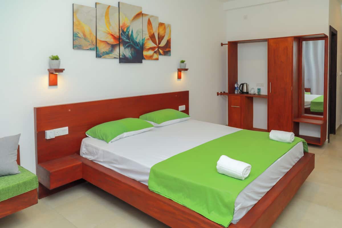 Une chambre d’hôtel bien aménagée, avec un grand lit, une literie verte et blanche, une armoire en bois et deux appliques murales.