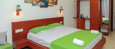 A neatly arranged hotel room with a large bed, green and white bedding, a wooden wardrobe, and two wall-mounted light fixtures.