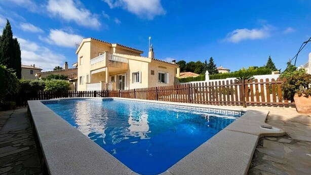 Ein Schwimmbecken mit Holzzaun, ein Gebäude mit Balkon und ein klarer, blauer Himmel.