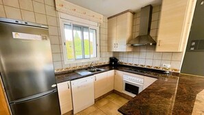 Eine Küche mit Edelstahl-Kühlschrank, weißen Schränken, einem Fenster und einer Arbeitsplatte aus Stein.