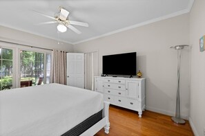 Un dormitorio con cama, televisor sobre una cómoda, ventilador de techo y lámpara de pie.