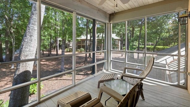 A covered outdoor area with large windows, wooden furniture, and a ceiling fan.