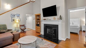 A living room with a fireplace, a television mounted above it, a sofa, a coffee table, and a bookshelf.