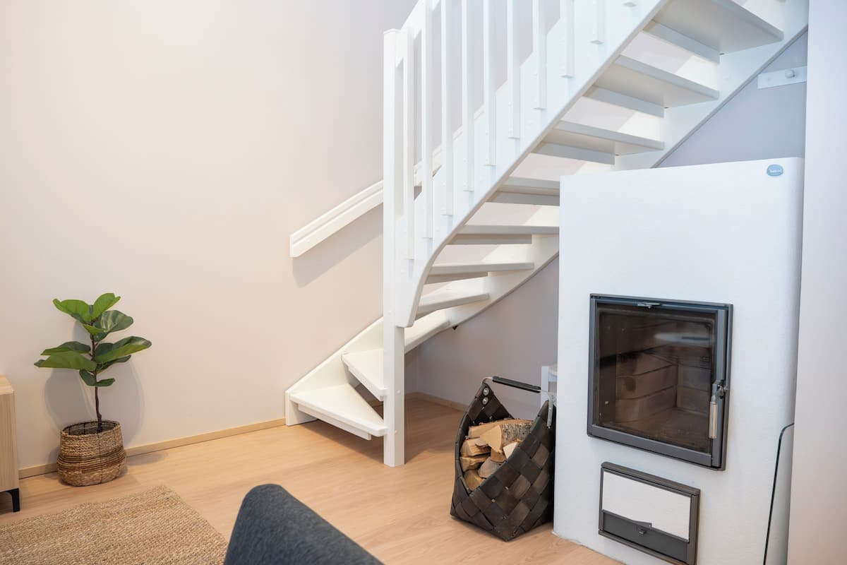 A modern apartment with a white staircase, a built-in fireplace, a potted plant, and a wicker basket.
