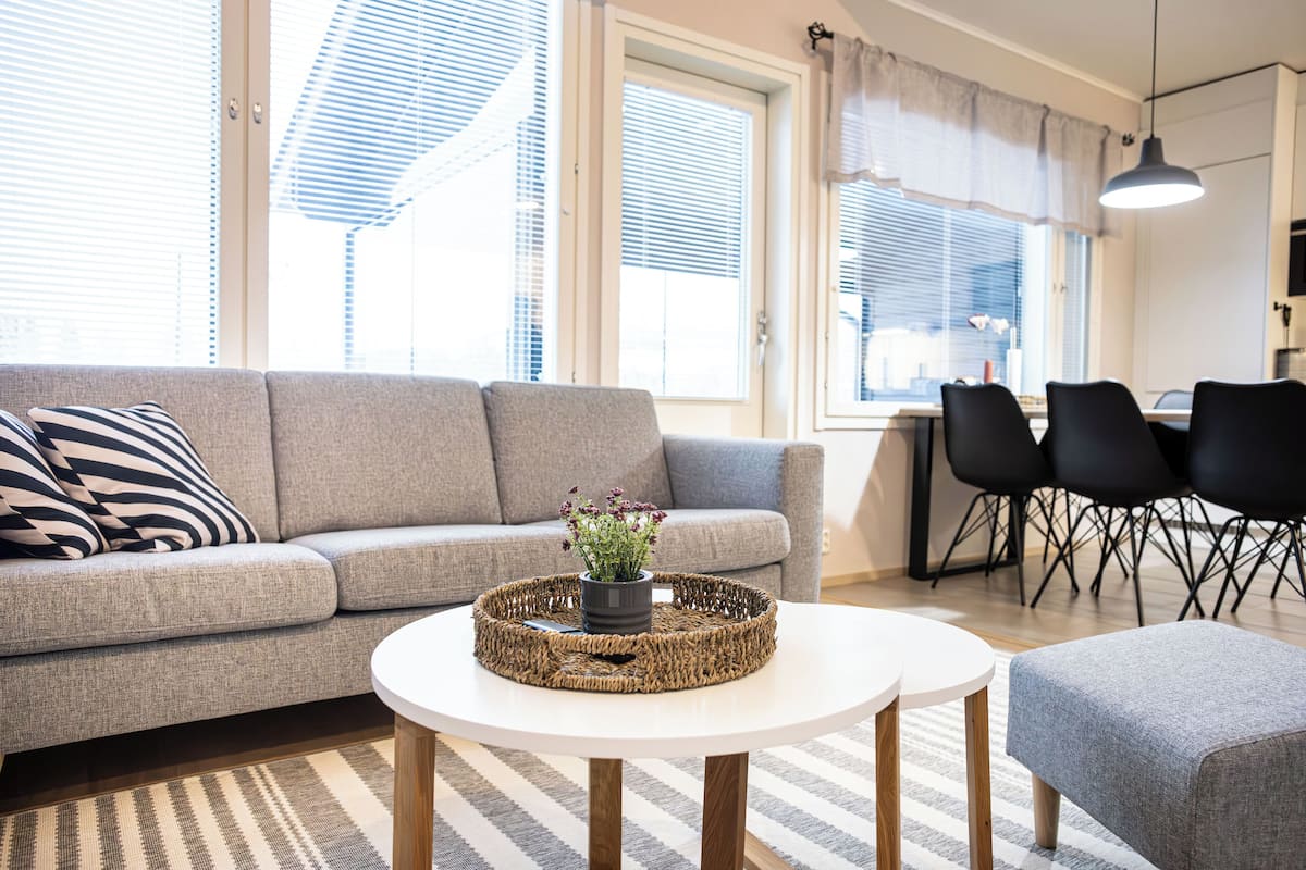 A modern living room with a grey sofa, a round white coffee table, and a grey ottoman. There is a wicker tray with a plant on the coffee table.