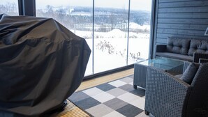 Una sala de estar moderna con una mesa de centro de vidrio, un sofá y un sillón informal con funda. Un ventanal ofrece vistas a un paisaje nevado.