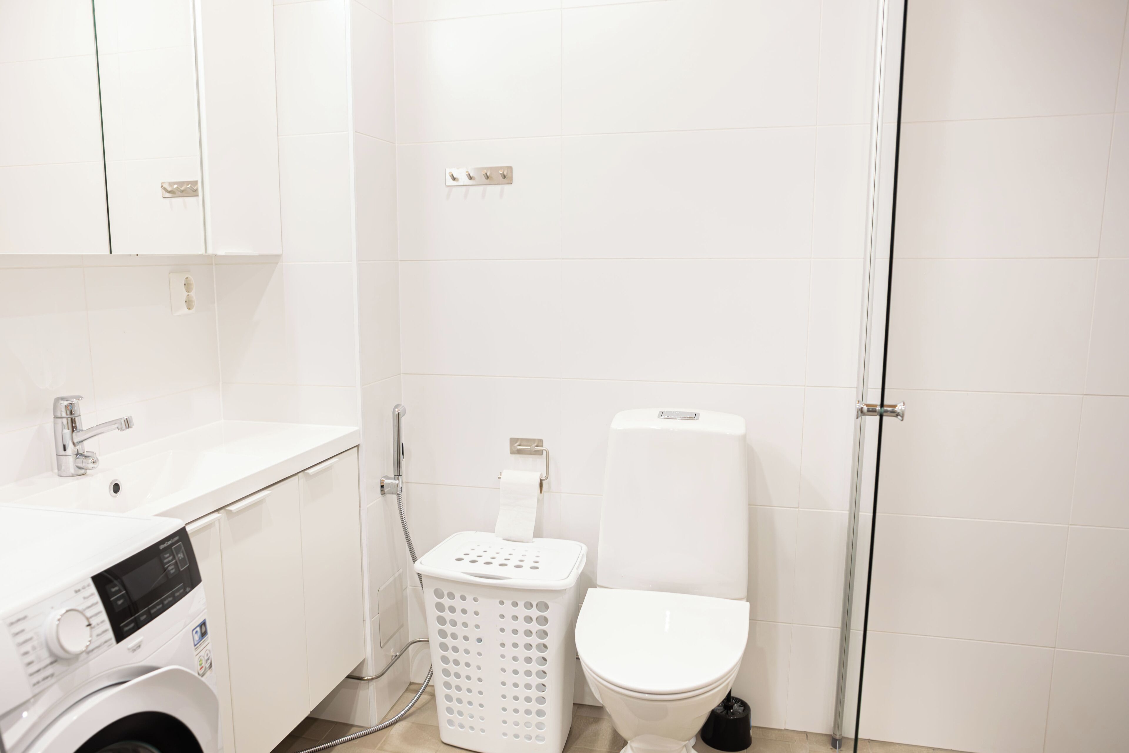 A compact bathroom with a washing machine, a toilet, and a shower.