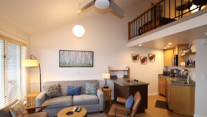 En moderne stue med sofa, stole, et sofabord og et køkkenområde med en bordplade og hårde hvidevarer.