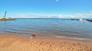 En strand med klart, blåt vand, en båd ligger til højre, og en kran til venstre.