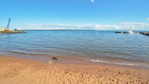 A beach with clear blue water, a boat docked on the right, and a crane on the left. - Bayfield Condo 1BR + Loft | Lake Superior View (Bayfield)