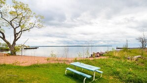 A picnic table in a grassy area with a lake and a dock in the background. - Bayfield Condo 1BR + Loft | Lake Superior View (Bayfield)