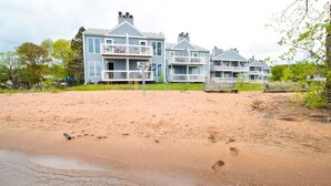 A beachfront property with a large house featuring multiple balconies and a sandy beach in the foreground. - Bayfield Condo 1BR + Loft | Lake Superior View (Bayfield)