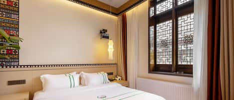 Une chambre d’hôtel avec un lit bien fait, une table de chevet avec une lampe, un radiateur et une fenêtre ornée de vitraux décoratifs.