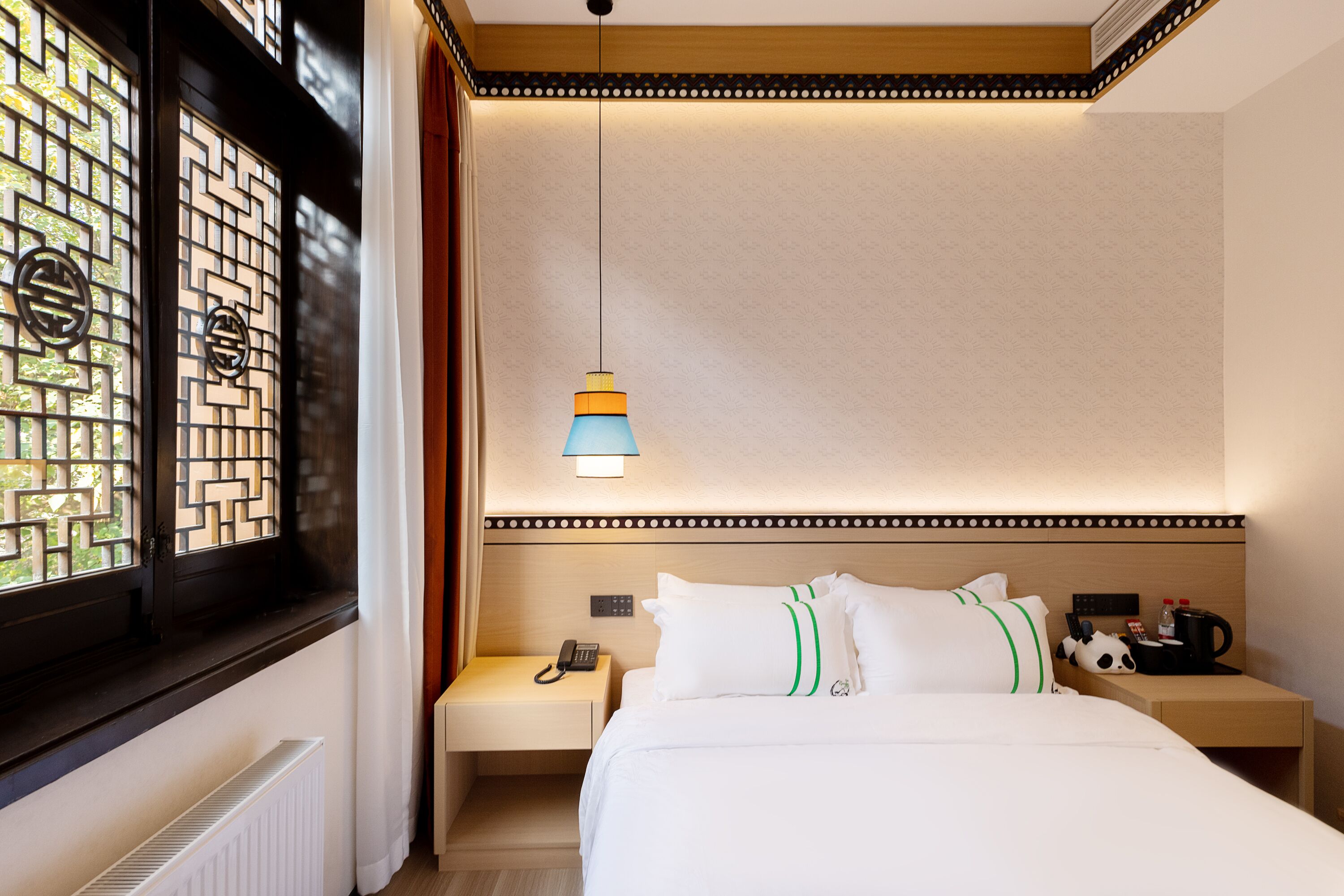 A hotel room with a bed, bedside tables, a nightstand, a lamp, and a window with decorative shutters.