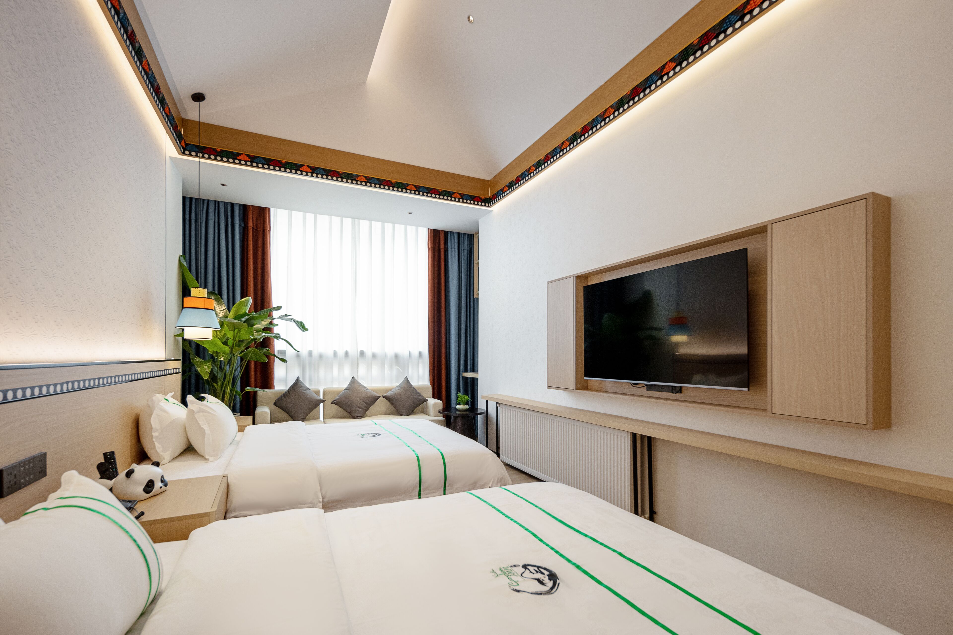 A hotel room with two beds, a TV, a plant, and a window with curtains.